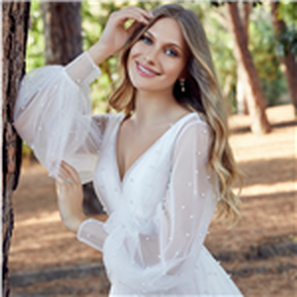 Close up of a bride stood in woodland wearing a white wedding dress with long sheer detachable pearl-beaded blouson sleeves